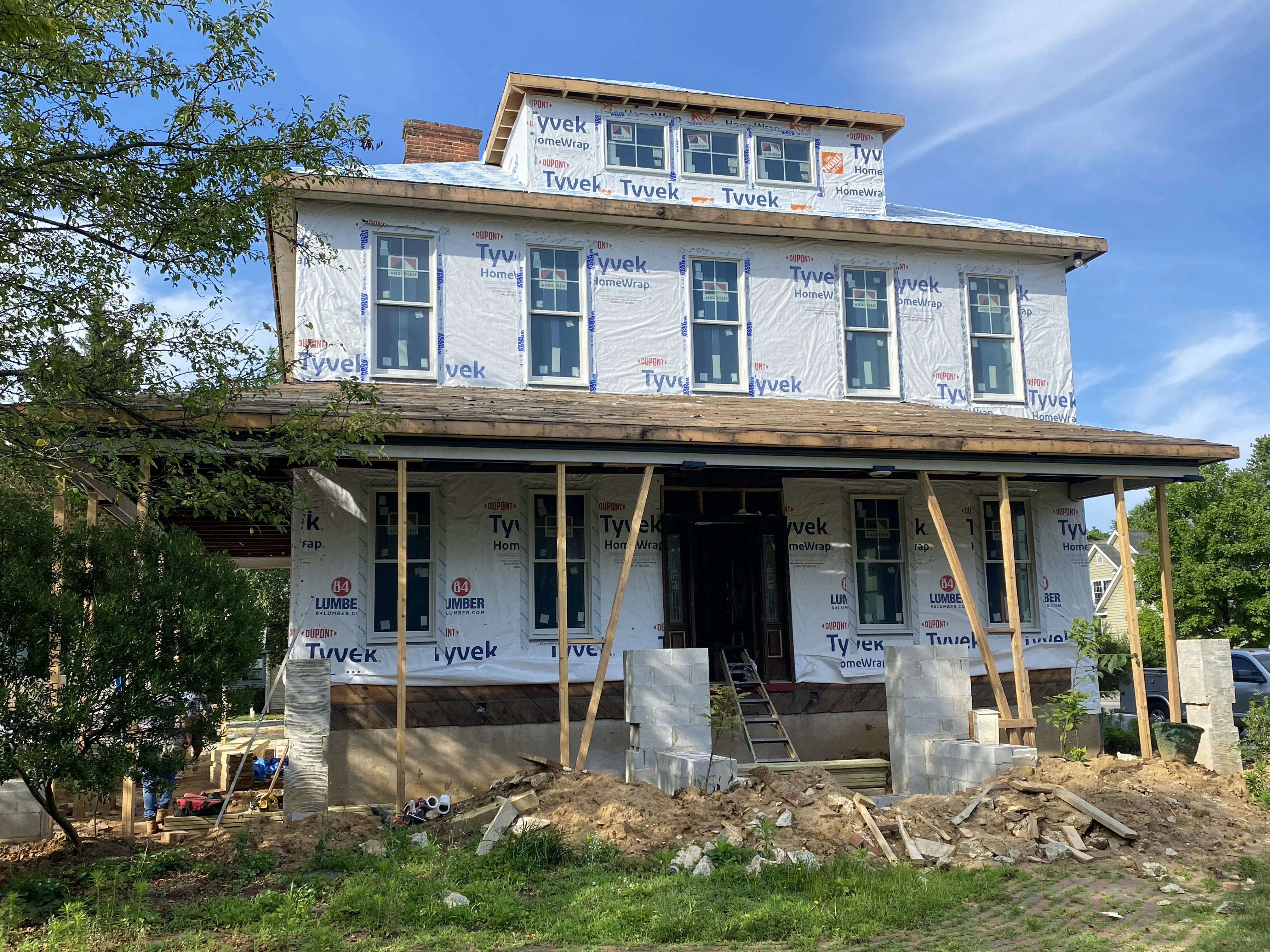 Two-story home under renovation with new roof framing, Tyvek house wrap, and replacement windows installed