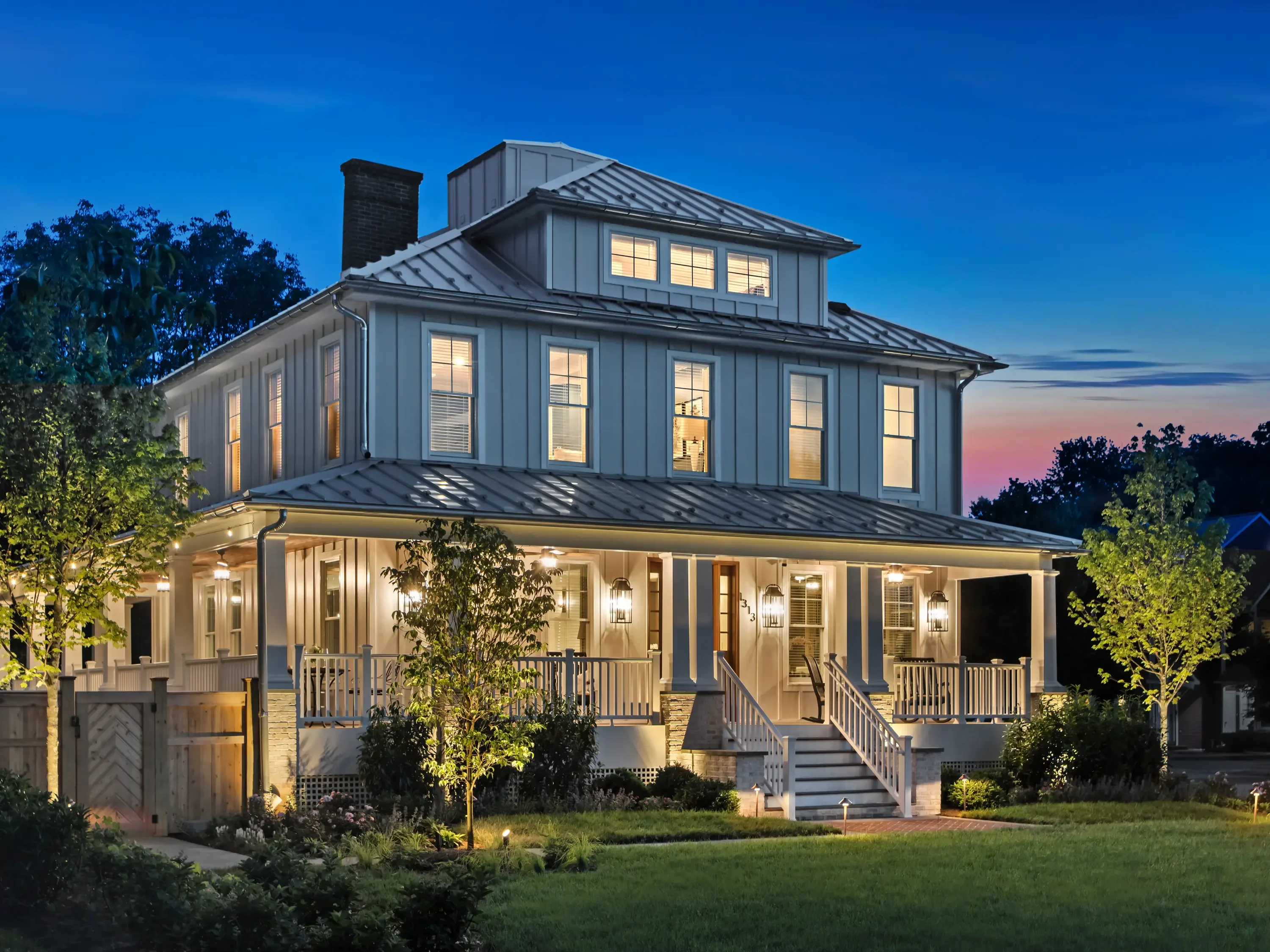Standing seam metal roof with multiple peaks, brick chimney, and integrated exterior lighting on modern farmhouse