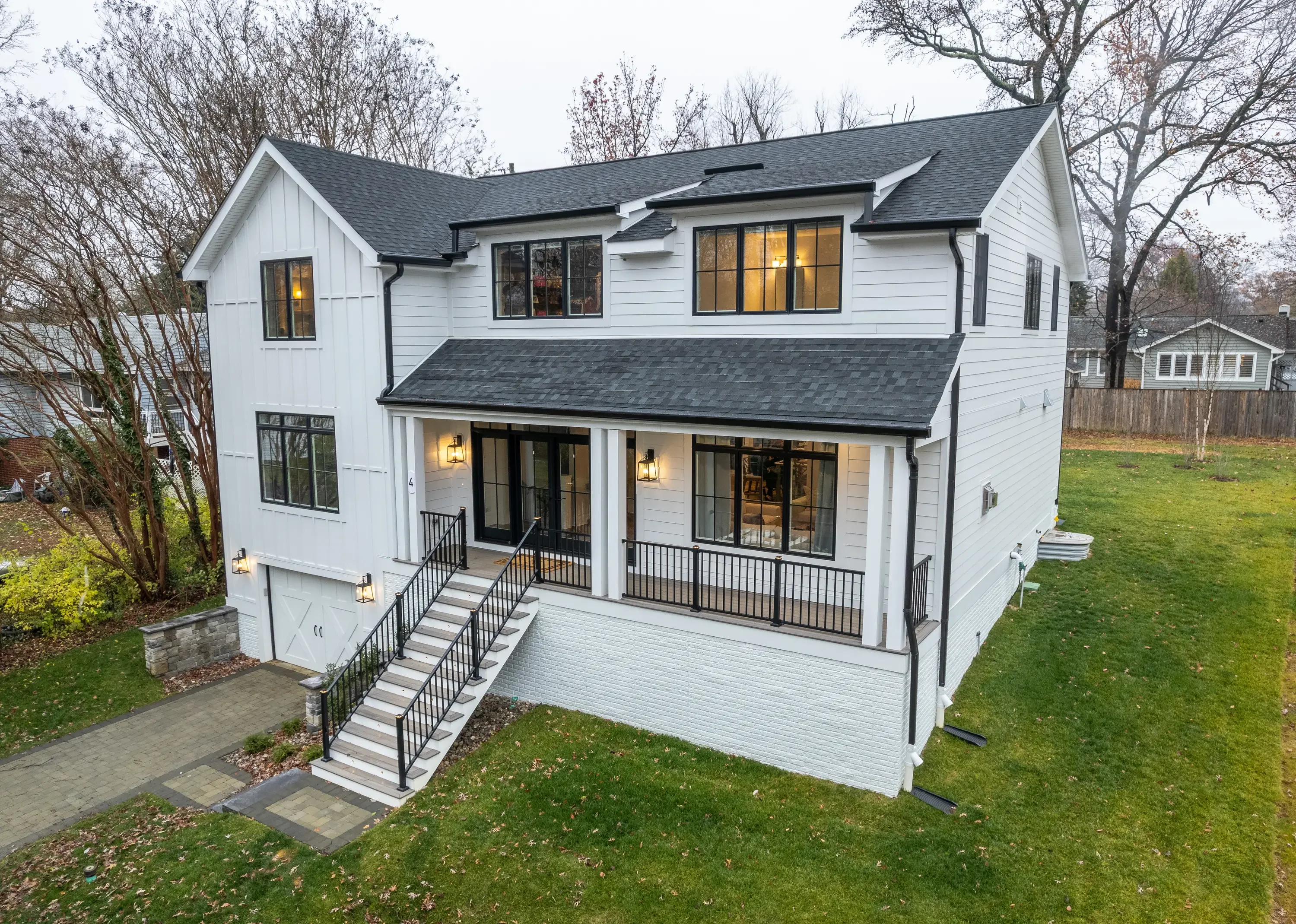 Two-story white farmhouse with charcoal gray dimensional shingle roof, black trim, and covered porch with metal railings